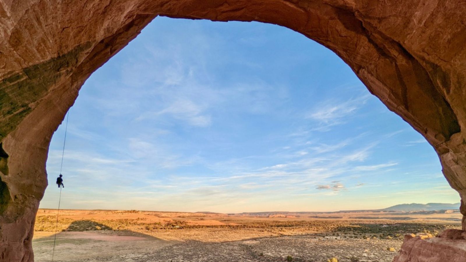 climbing in moab a person rappels behind a large rock arch formation at sunset