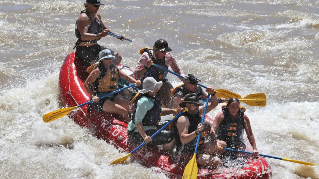 moab tours A red raft filled with people with paddles navigates white water